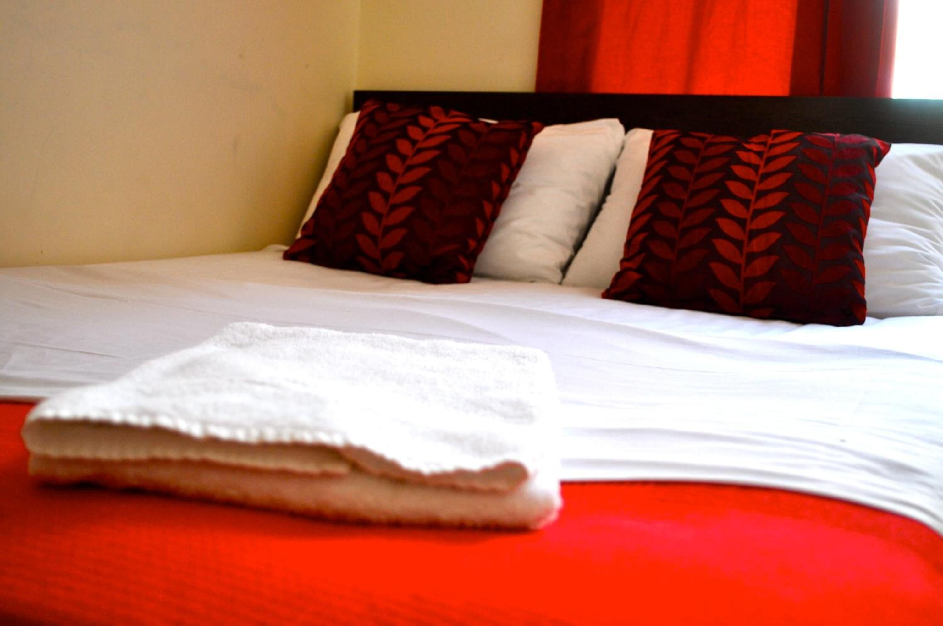 Una cama bien hecha con sábanas blancas y dos almohadones decorativos con diseño de hojas.