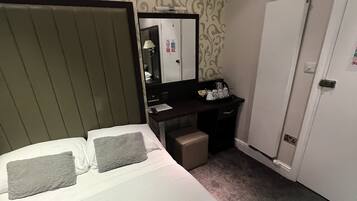 Una habitación de hotel con una cama, un escritorio, un espejo y una puerta.