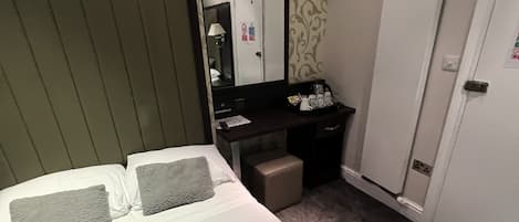 A hotel room with a bed, a desk, a mirror, and a door.