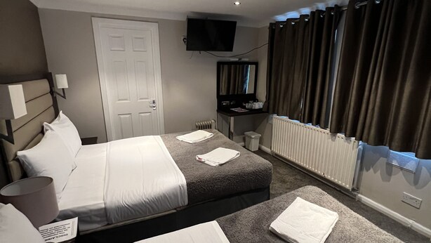 A hotel room with two beds, a television, a mirror, and a window with curtains. - Goodwood Hotel (London)