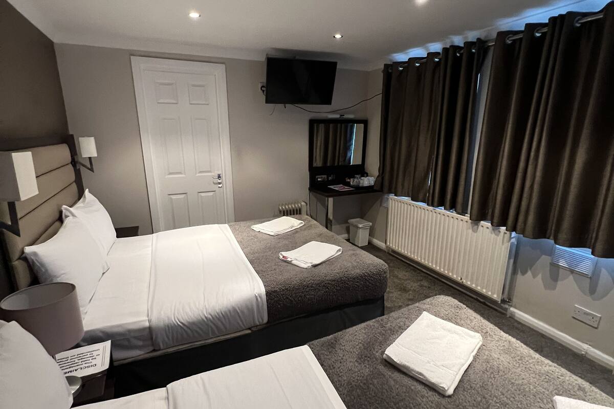 A hotel room with two beds, a television, a mirror, and a window with curtains.