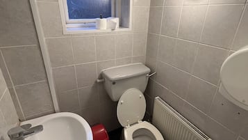 A small bathroom with a toilet, a sink, and a window.