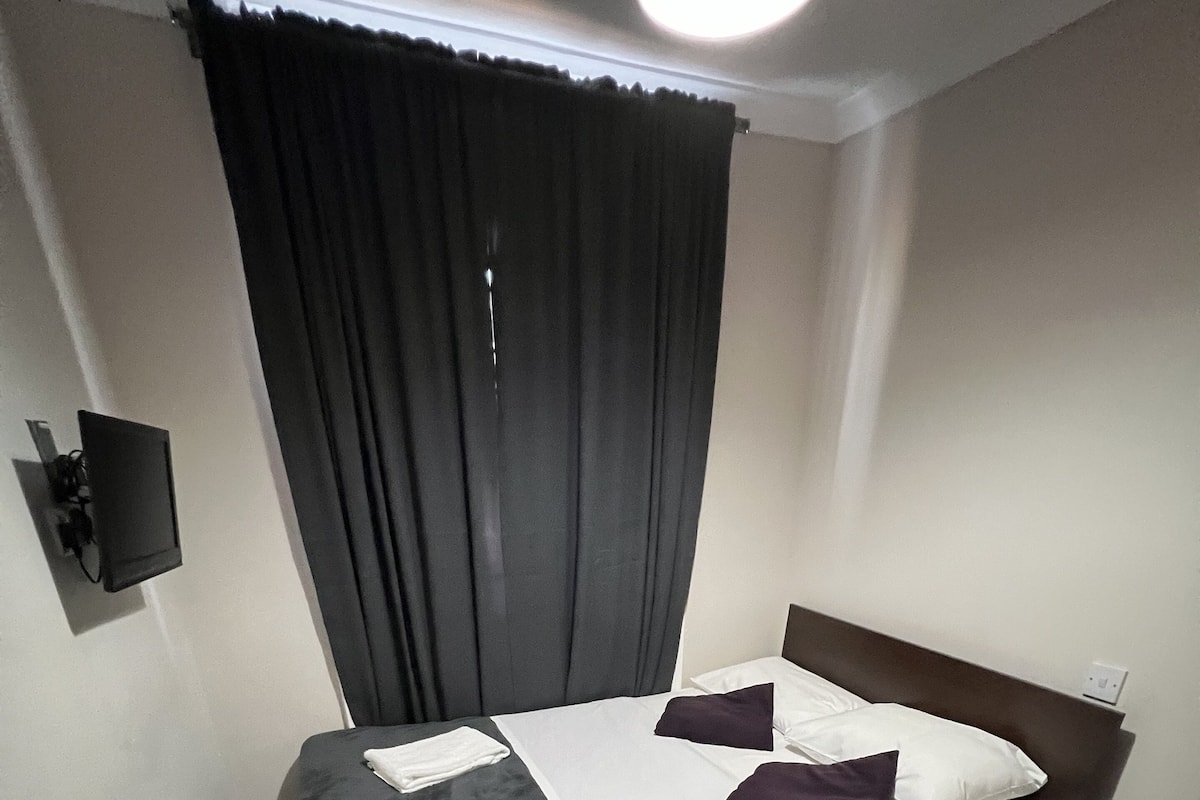A neatly made bed with white and dark bedding, a dark headboard, and a small bedside table.