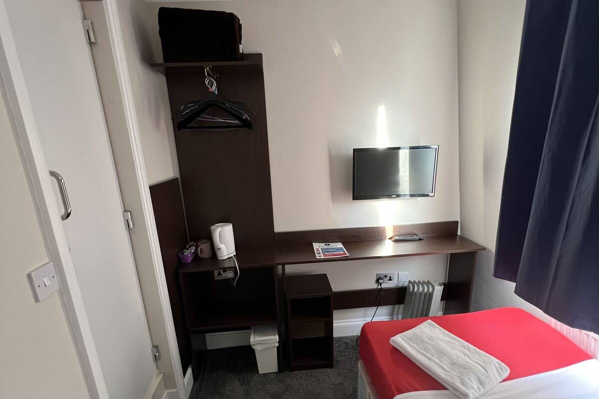 A hotel room with a bed, a desk, a chair, a TV, and a wardrobe.