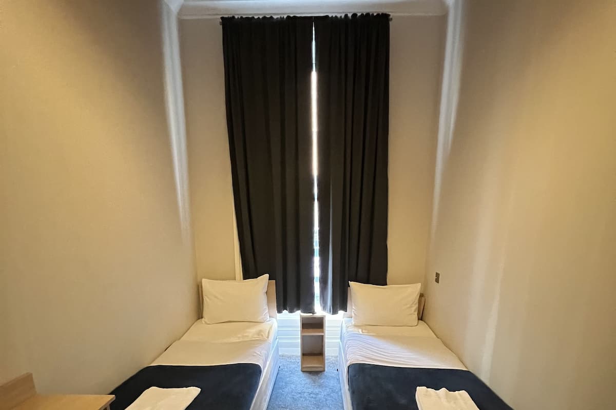 A small, compact room with two single beds, a small table, and a radiator.