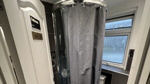 A bathroom with a glass shower enclosure, a toilet, and a window. - Goodwood Hotel (London)