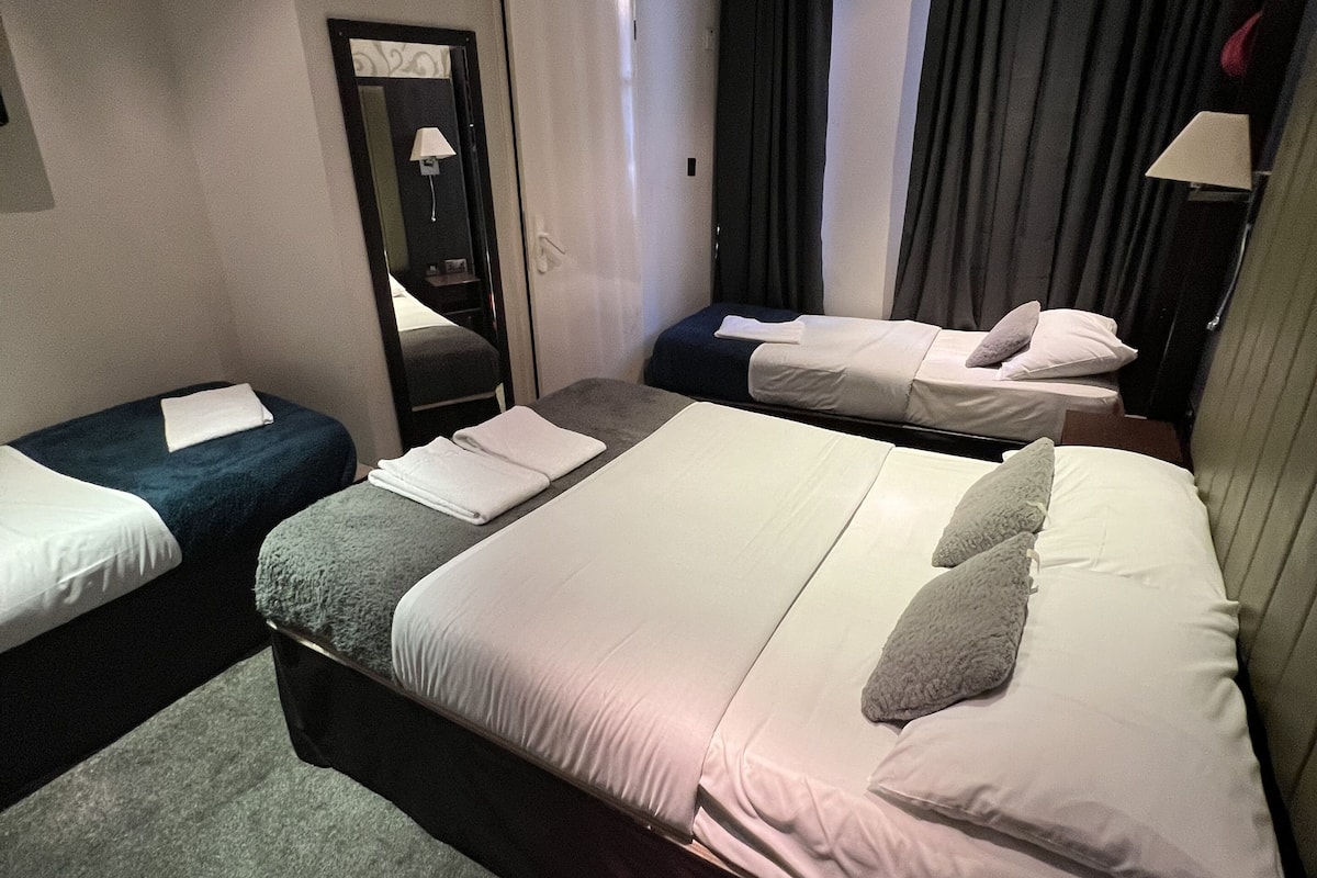 A hotel room with a large bed, two smaller beds, a mirror, a door, and a window with curtains.