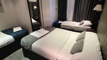 Una habitación de hotel con una cama grande, dos camas más pequeñas, un espejo, una puerta y una ventana con cortinas.