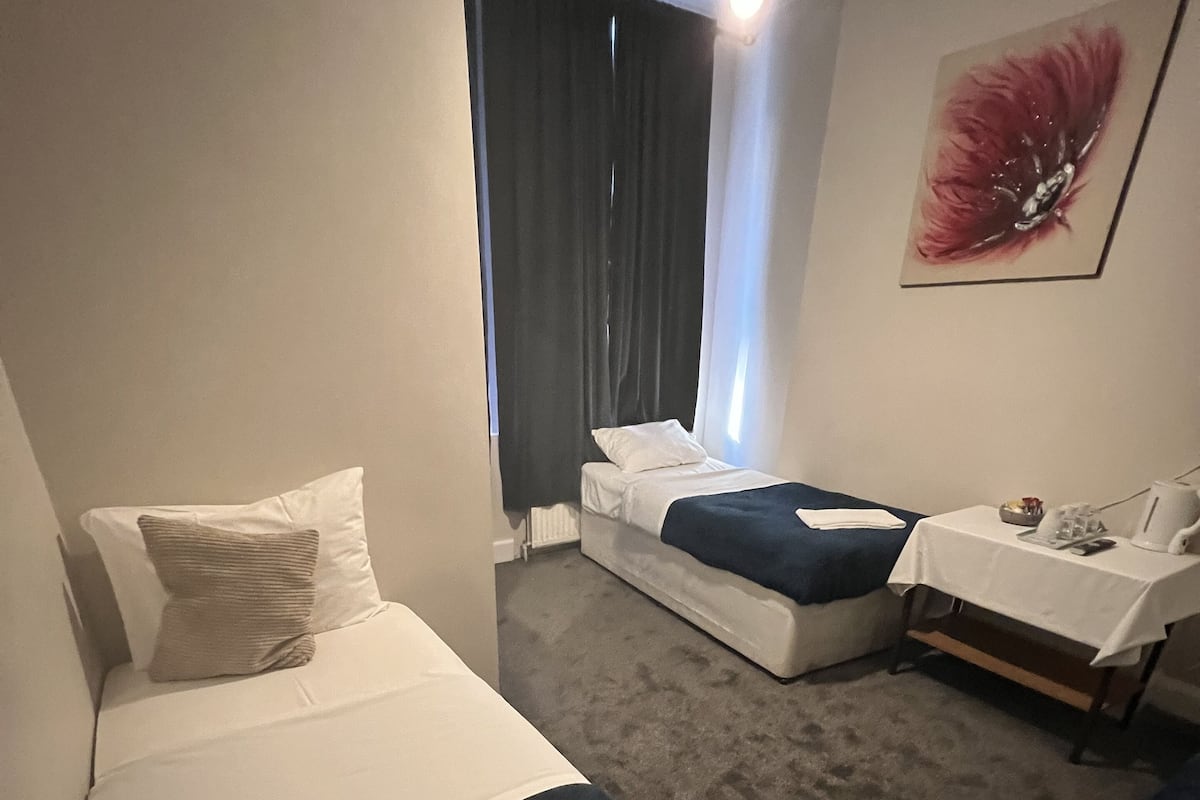 A hotel room with a bed, a bedside table with a lamp, a chair, and a window with curtains.