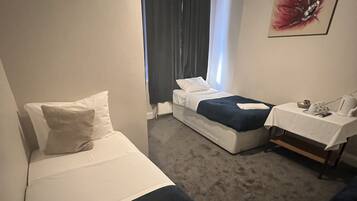 Habitación de hotel con cama, mesita de noche con lámpara, una silla y ventana con cortinas.