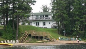 A lakeside property with a wooden dock, a small boat, and a building with a green roof.