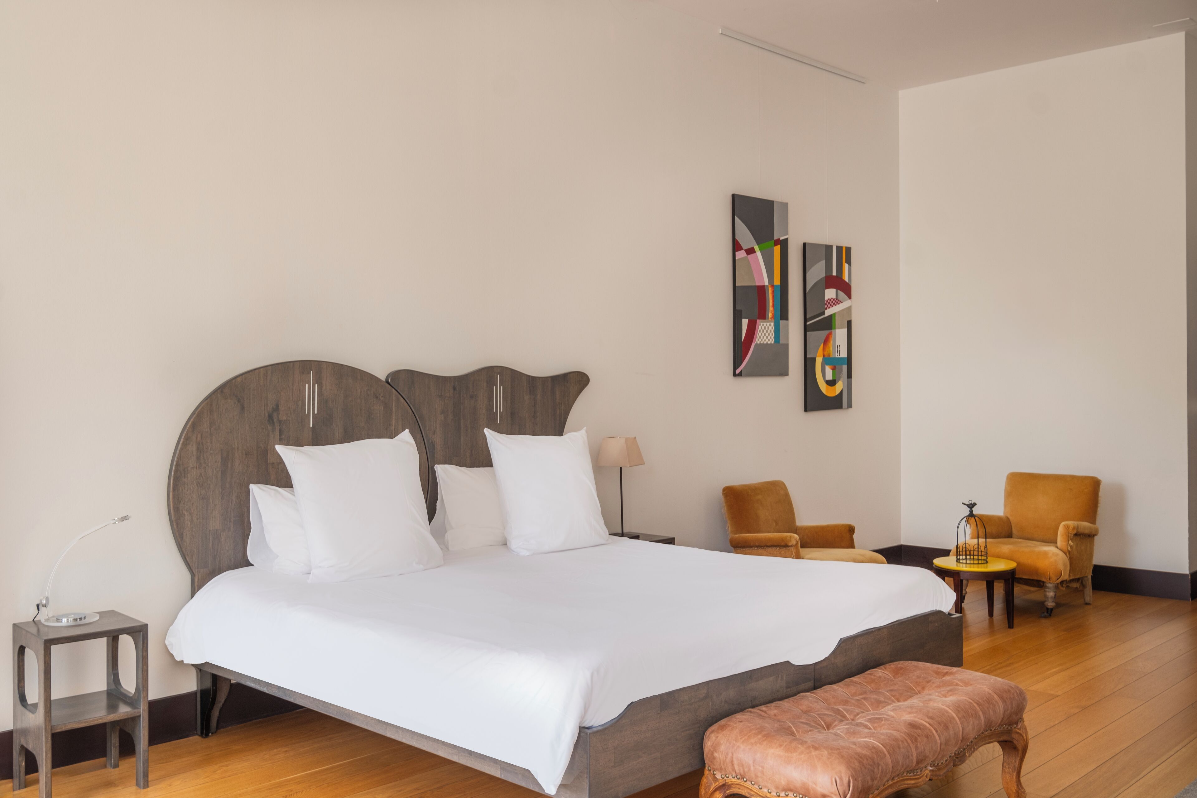 Una habitación de hotel moderna con una cama grande, dos sillones, una mesita y arte abstracto en la pared.
