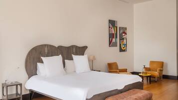 Una habitación de hotel moderna con una cama grande, dos sillones, una mesita y arte abstracto en la pared.
