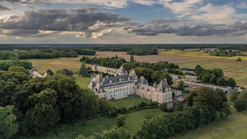 Un vaste domaine comprenant plusieurs bâtiments, entouré d’une végétation luxuriante et de champs.