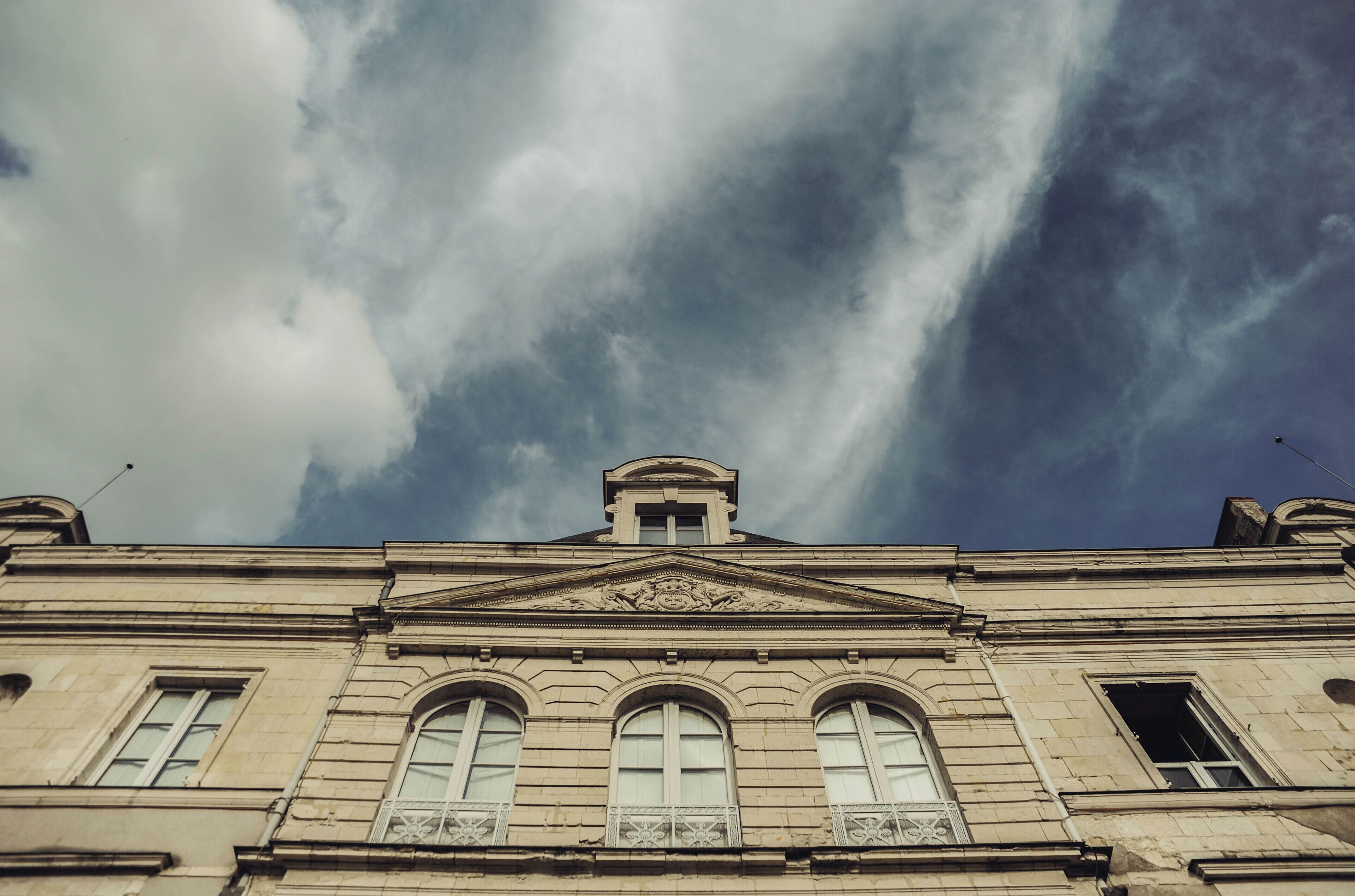 A classical building with a prominent central pediment and three arched windows.