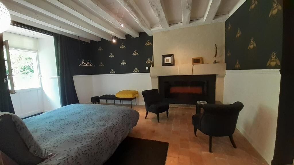 Un dormitorio con cama, dos sillas, chimenea y ventana.