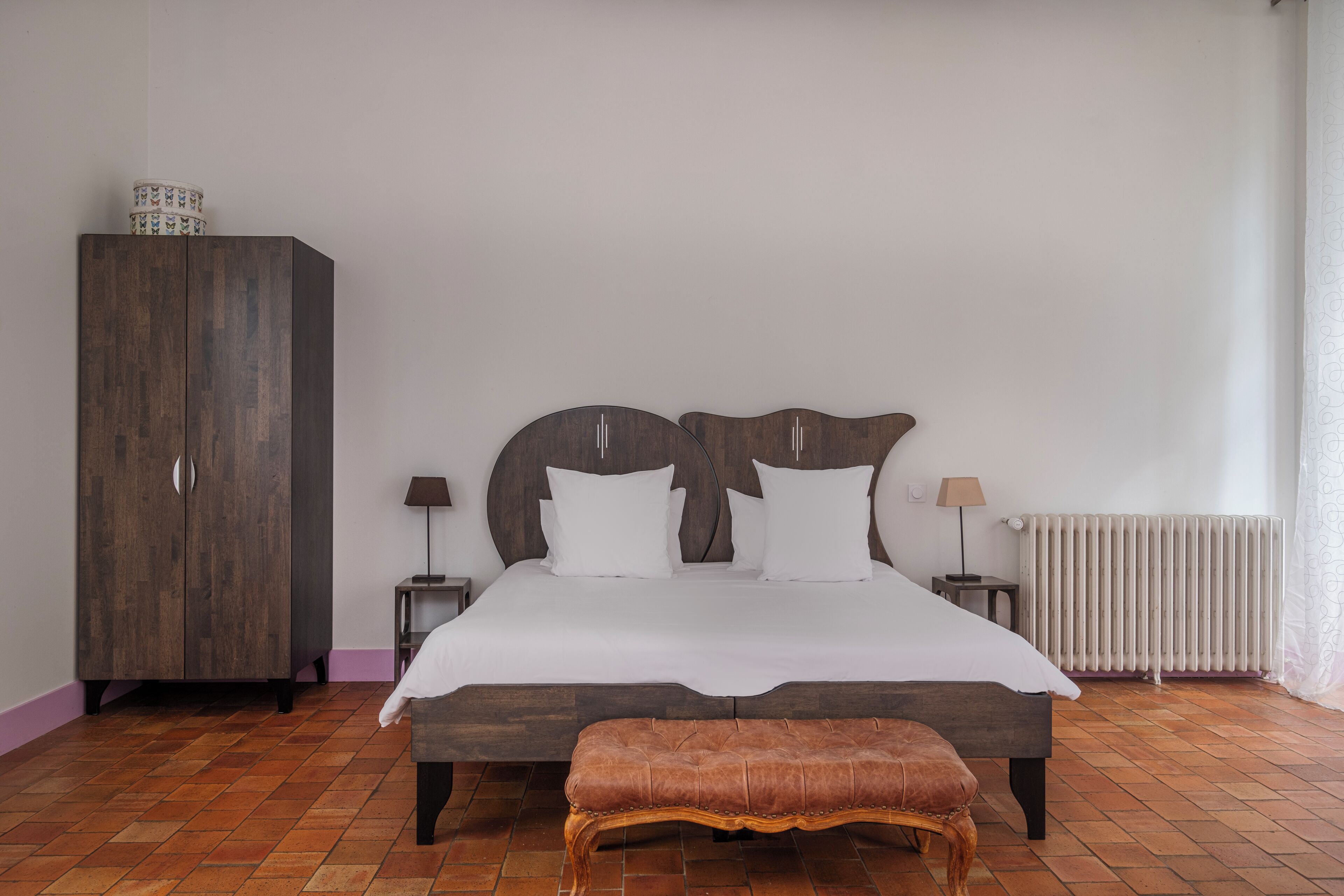 A bedroom with a large bed, a wooden wardrobe, a bench, and a radiator.