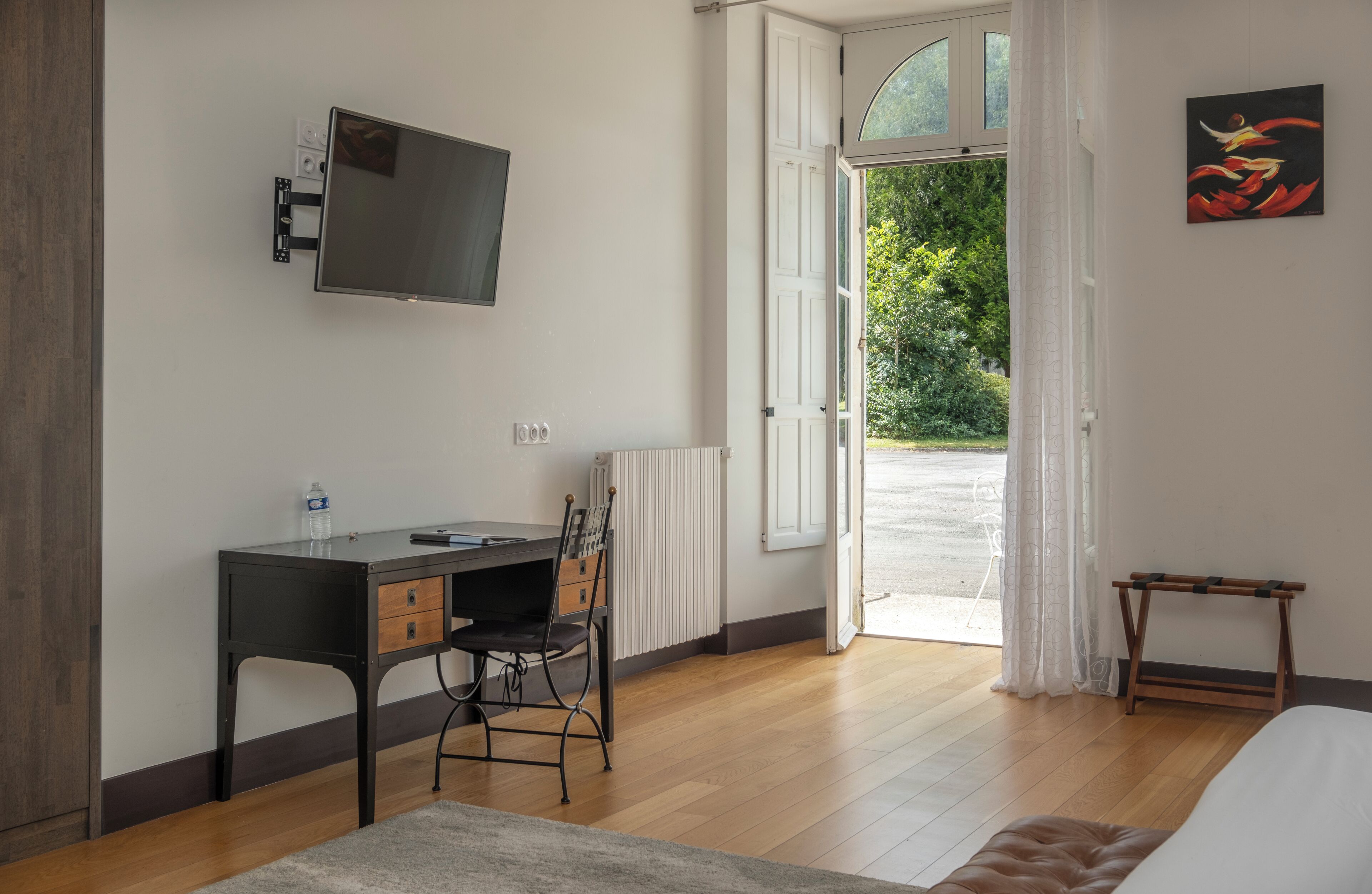 Un dormitorio con cama, escritorio con silla, televisor montado en la pared y ventana con cortinas.
