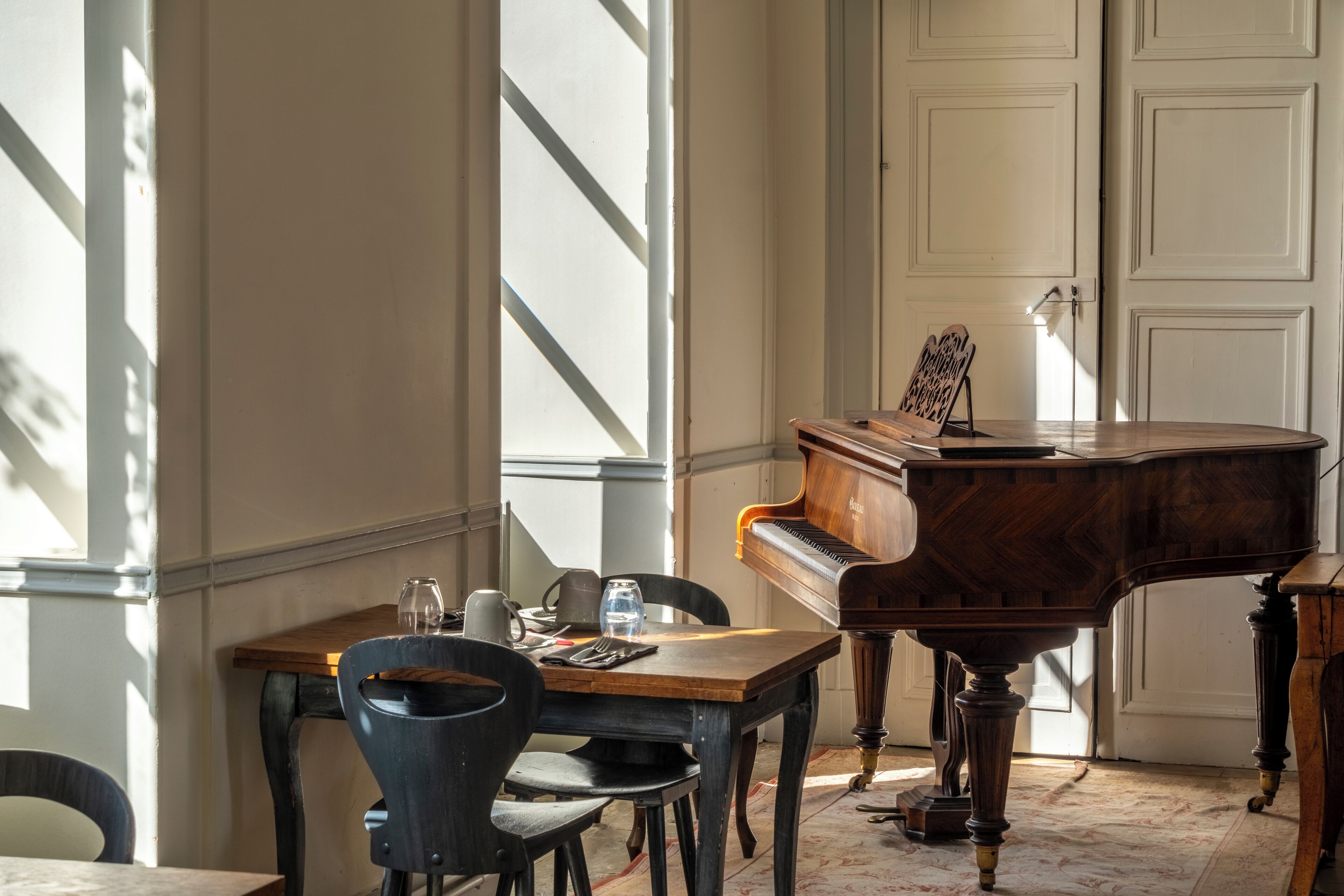 A room with a grand piano, a dining table with chairs, and a window with natural light.