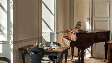 A room with a grand piano, a dining table with chairs, and a window with natural light.