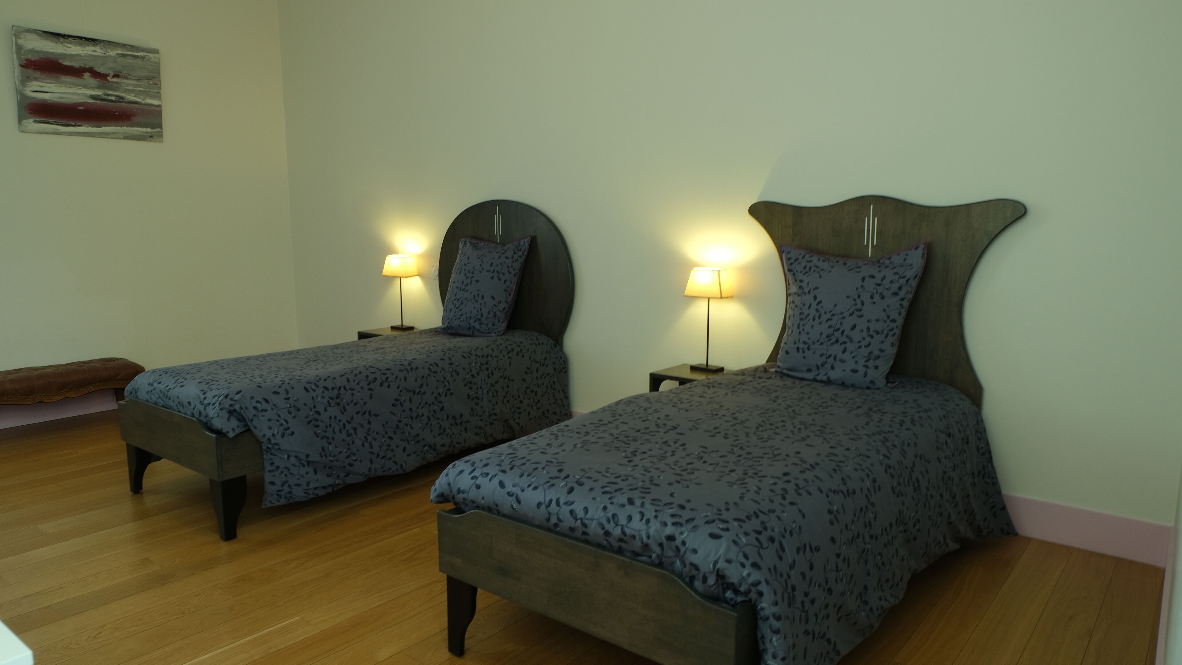 Two single beds with headboards, bedside tables, lamps, and a wooden floor.