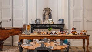 A dining area with a marble fireplace, a statue, and a variety of food and drink items on the table. - Château de Briançon, The Originals Relais (Loire-Authion)