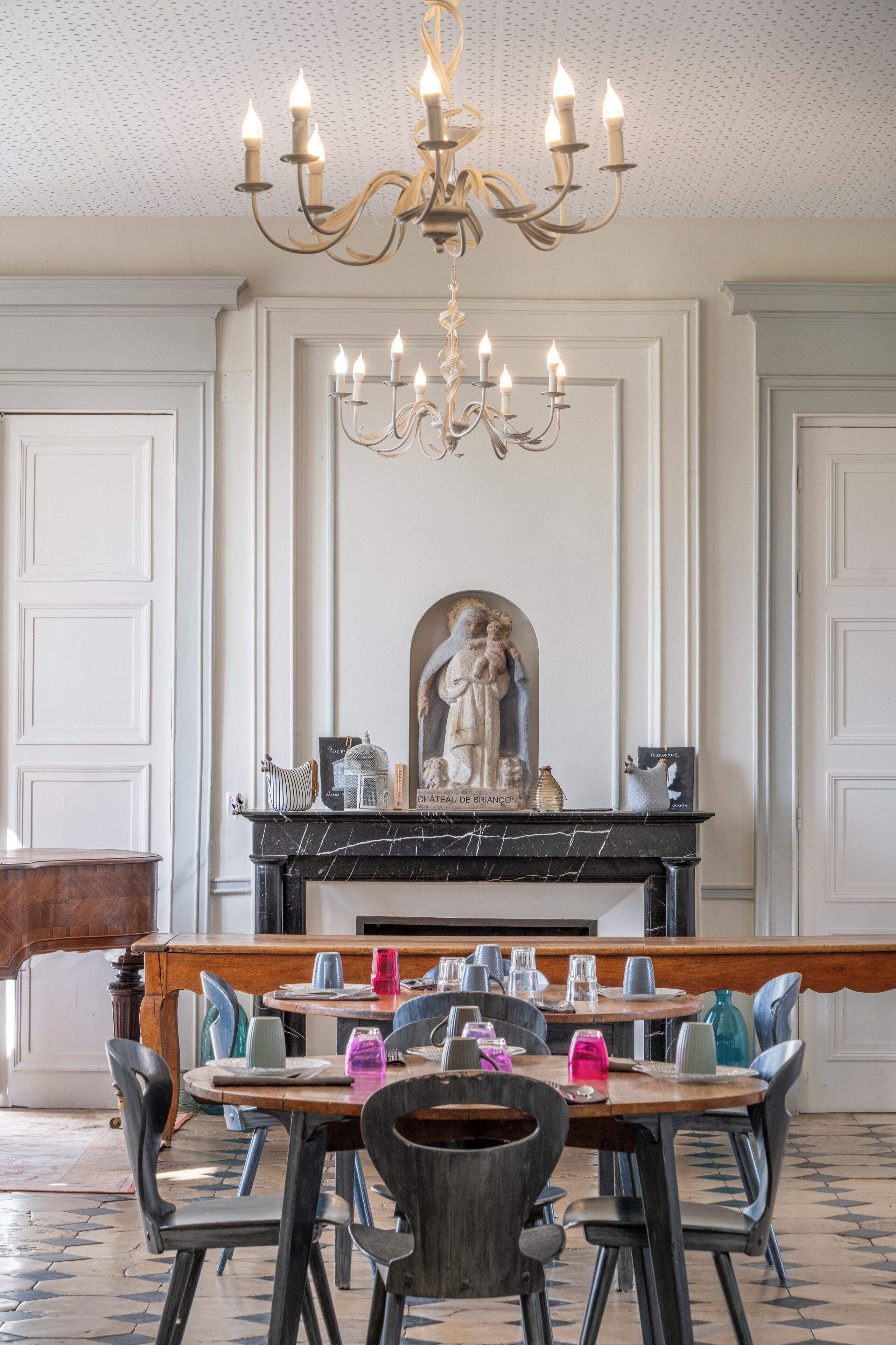 A dining area with a marble fireplace, a chandelier, and a statue.