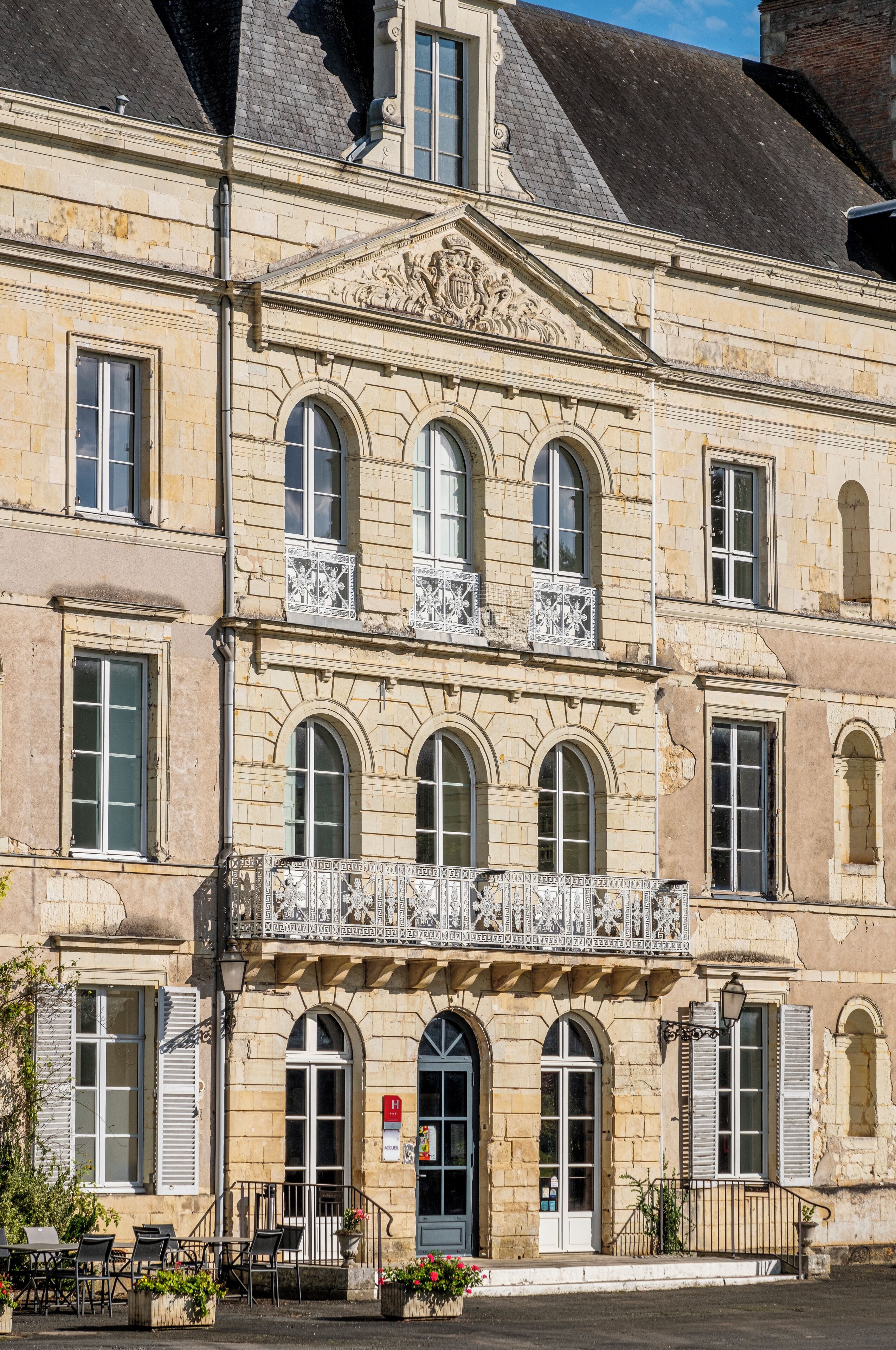 Un edificio histórico con múltiples ventanas, un balcón central con barandilla ornamental y una puerta con un letrero.
