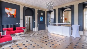 A spacious lobby with red seating, a white reception desk, and a patterned tile floor. - Château de Briançon, The Originals Relais (Loire-Authion)