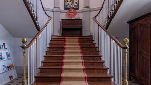 A grand staircase with a red carpet, flanked by white balustrades and gold balusters, leading to a landing with a wall of photographs. - Château de Briançon, The Originals Relais (Loire-Authion)