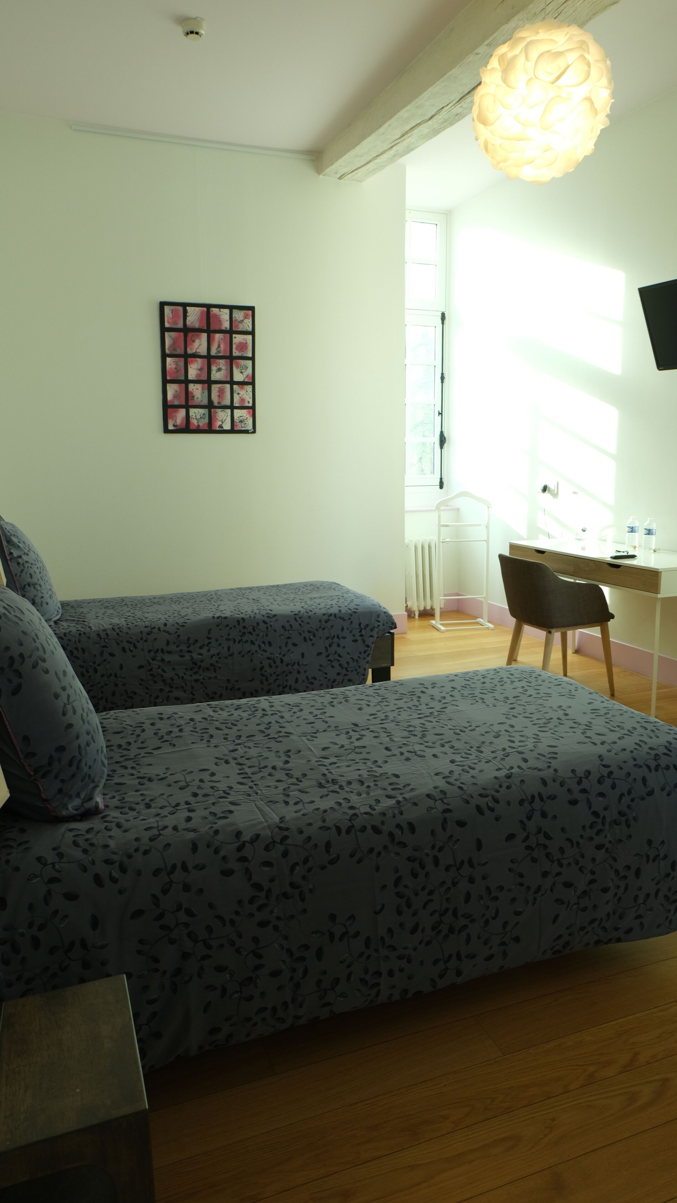 A bedroom with two beds, a desk, a chair, and a wall-mounted TV.