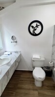 Un baño con lavamanos de mármol, inodoro y espejo montado en la pared.