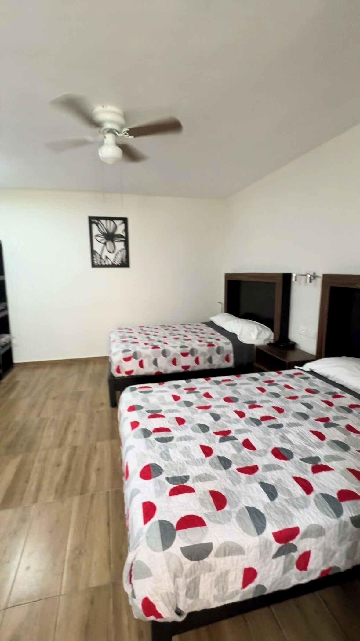A hotel room with two beds, a ceiling fan, and a wall art piece.