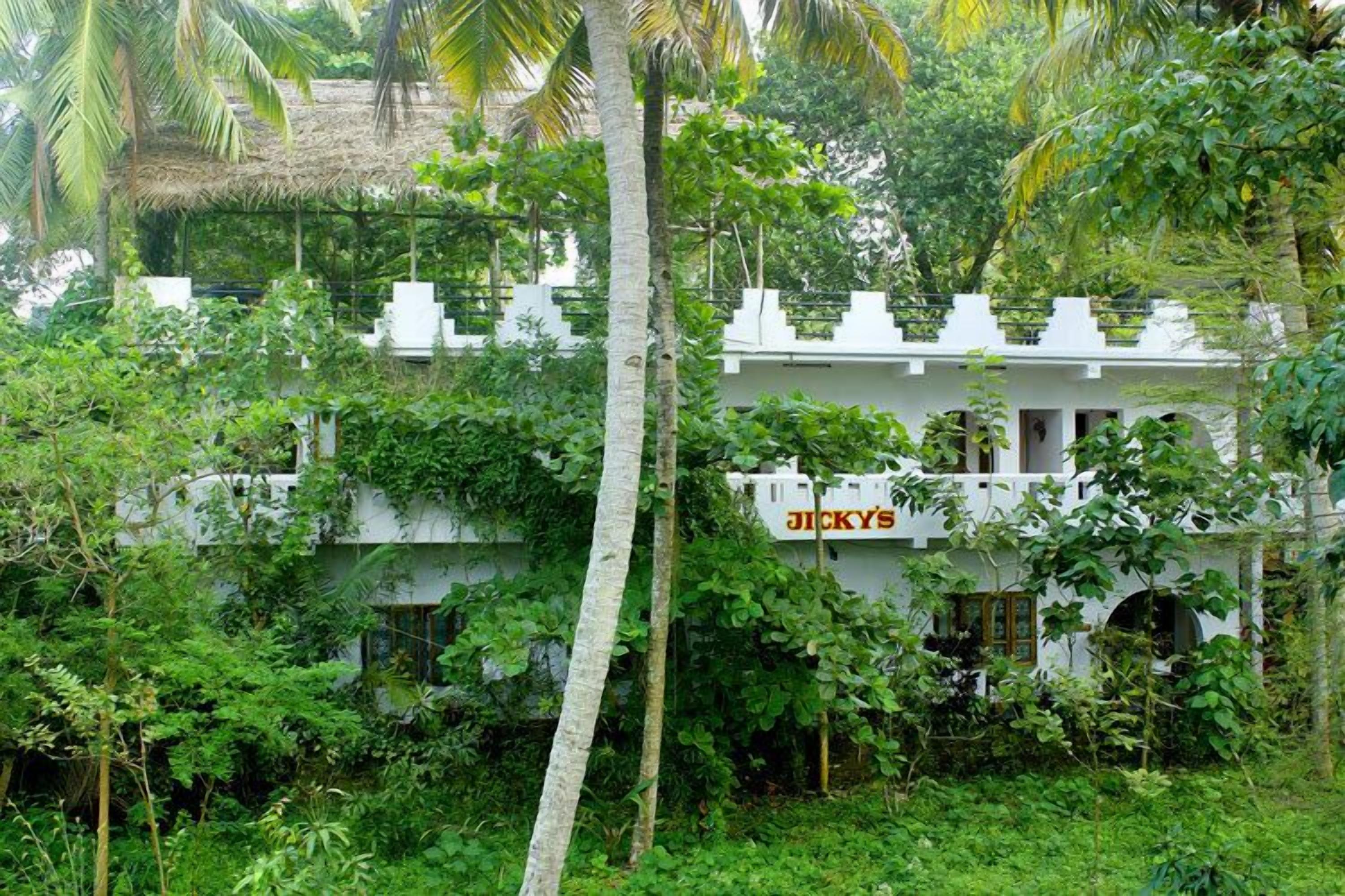 A white building with a sign reading "JICKY'S" partially obscured by dense green foliage.