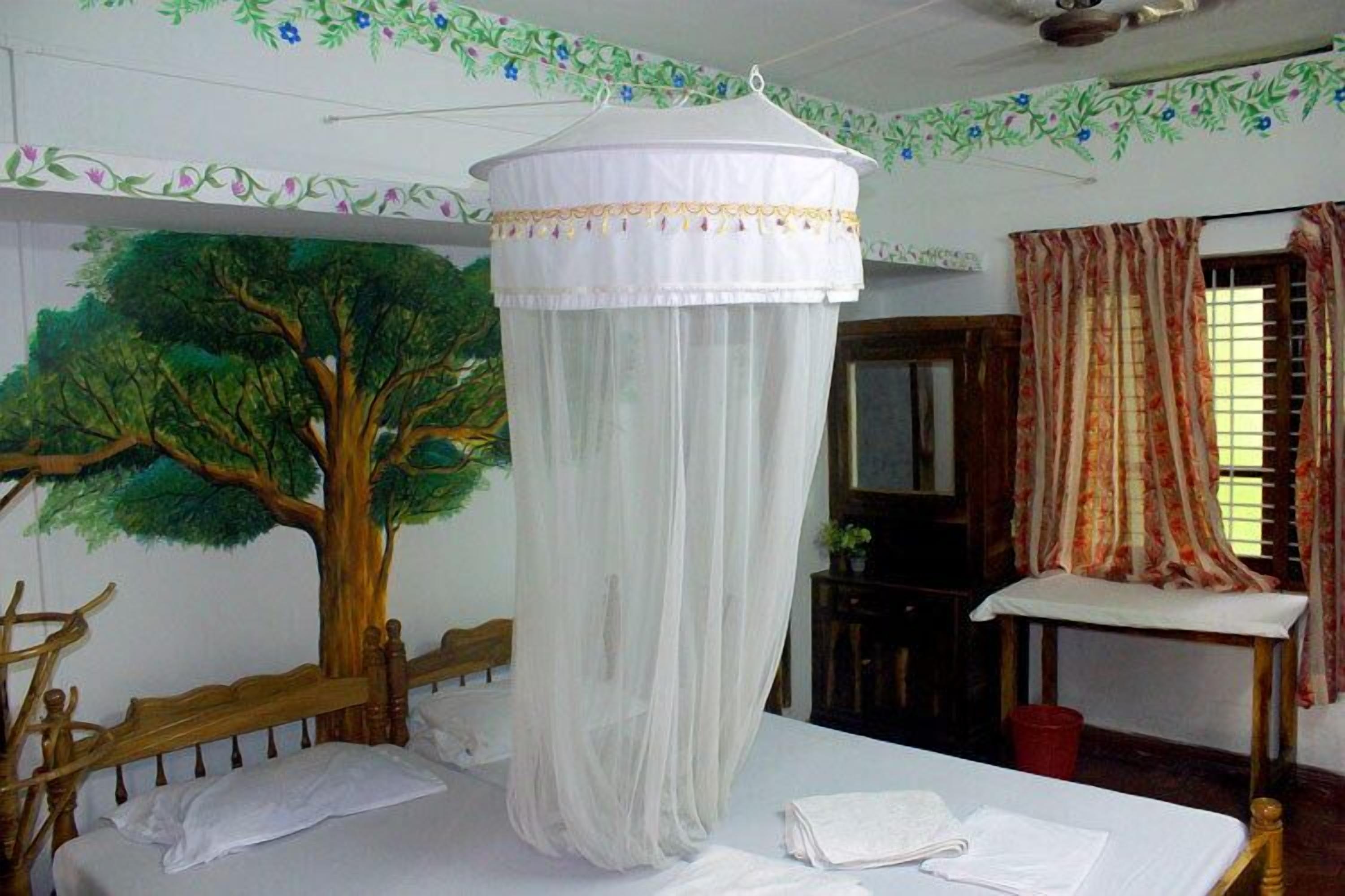 Una habitación con cama, dosel, cabecera de madera, mesita de noche, espejo y ventana con cortinas.
