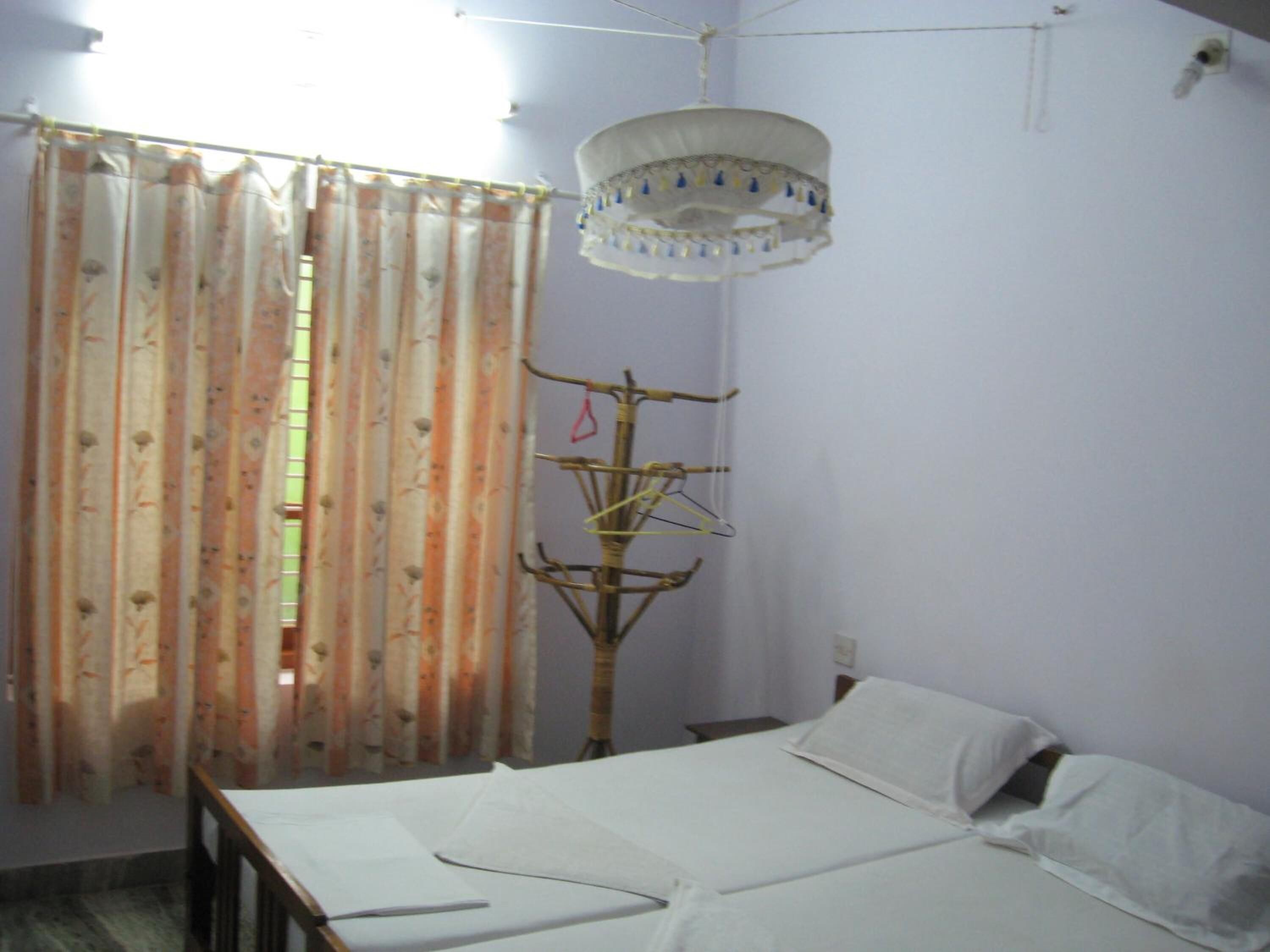 Quarto com cama, luminária pendente, varal de roupa e janela com cortinas.