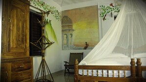 A room with a wooden bed, a tripod lamp, a chair, and a wall painting. - Jickys Nest (Varkala)