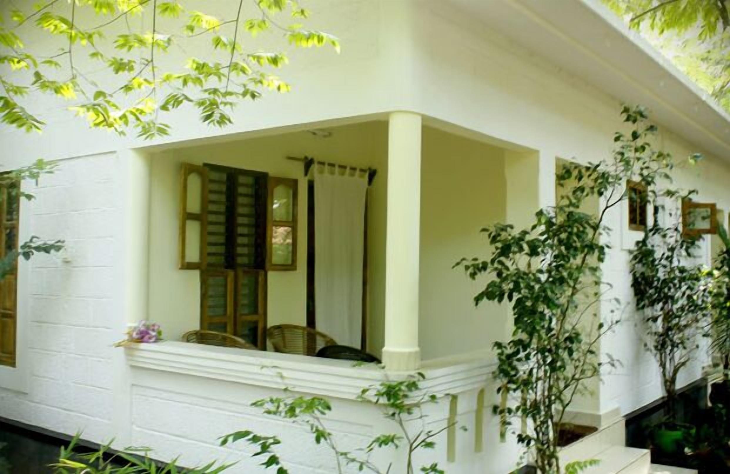 A white building with a covered porch, wooden shutters, and potted plants.
