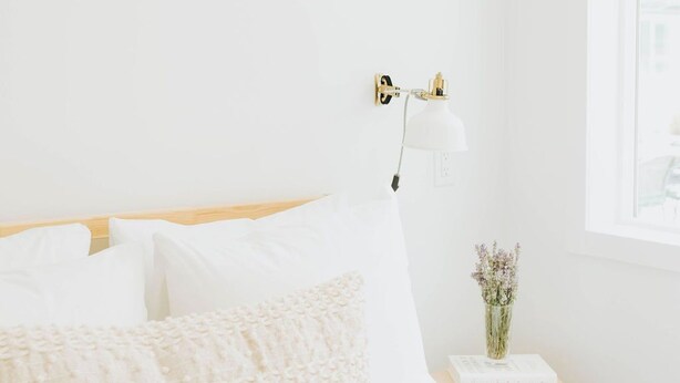 A minimalist bedroom with a bed, a bedside table with a lamp, and a framed picture on the wall. - Naramata Courtyard Suites (Naramata)