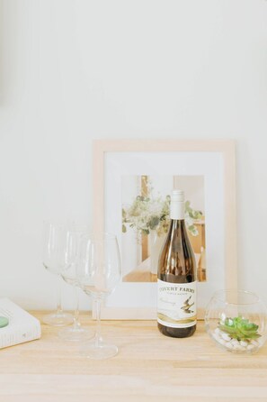 A bottle of wine, several empty wine glasses, a framed picture, and a small glass with white stones on a wooden surface. - Naramata Courtyard Suites (Naramata)