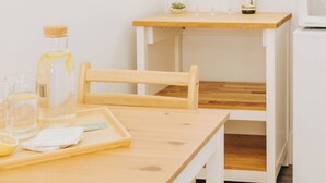 A kitchen with a wooden table, chairs, a small table with wine glasses, a bottle, and a microwave. - Naramata Courtyard Suites (Naramata)