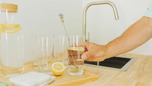 A hand holding a glass with a lemon slice and a sprig of lavender. - Naramata Courtyard Suites (Naramata)