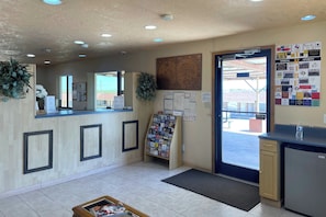 A reception area with a wooden counter, a bulletin board, a water dispenser, and a small refrigerator.