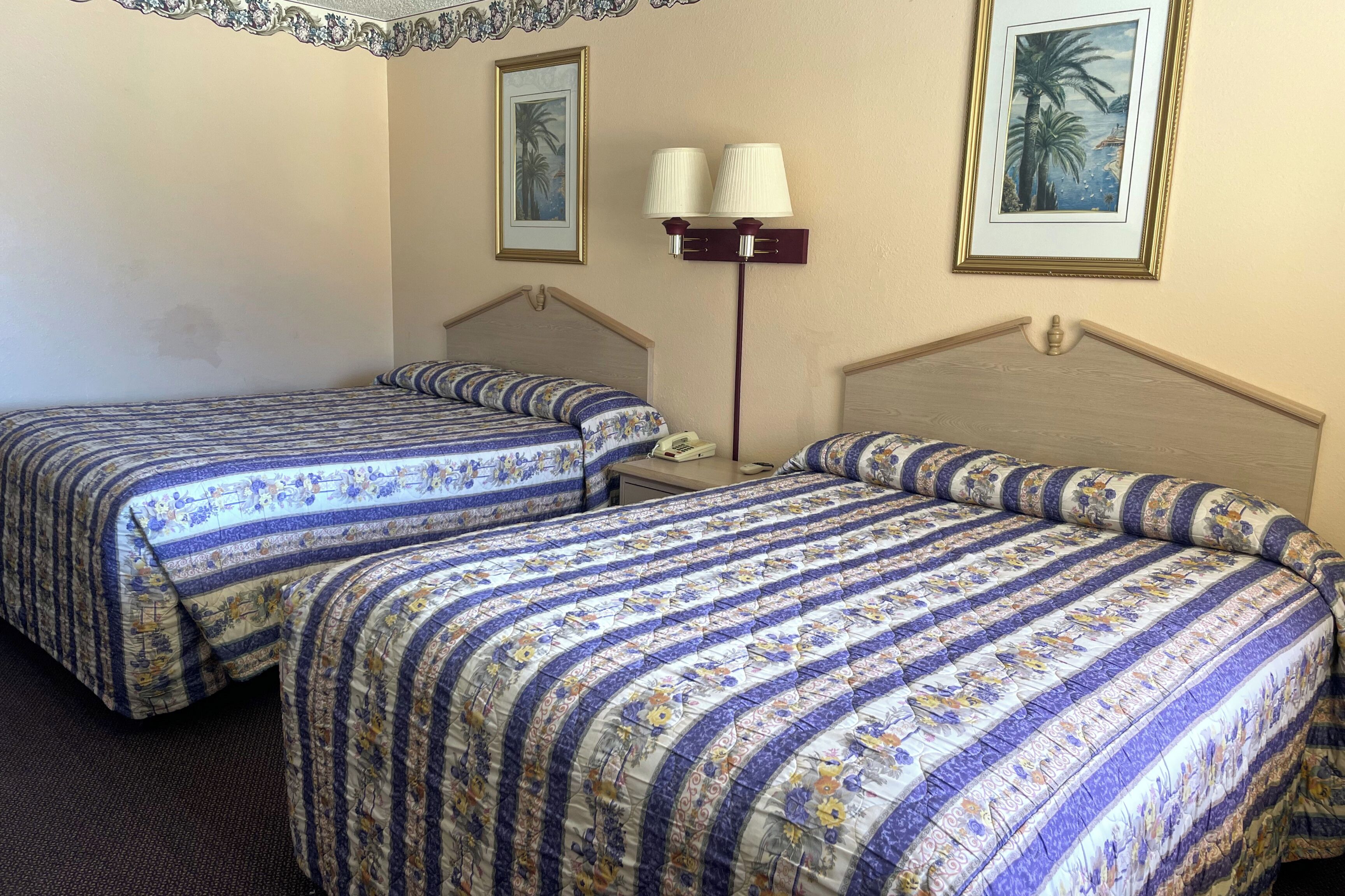 A hotel room with two beds, each with a floral-patterned bedspread, a nightstand with a lamp, and framed artwork on the walls.