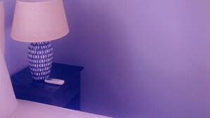 A bedroom with a ceiling fan, a painting of a beach scene, a lamp, and a nightstand. - Apartment Soleil (Soufrière)