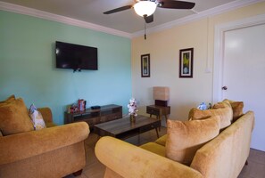A living room with a flat-screen TV, a ceiling fan, a coffee table, and a sofa. - Apartment Soleil (Soufrière)