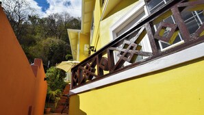 A yellow building with a staircase leading to a window with a wooden railing. - Apartment Soleil (Soufrière)