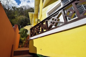 A yellow building with a staircase leading to a window with a wooden railing. - Apartment Soleil (Soufrière)