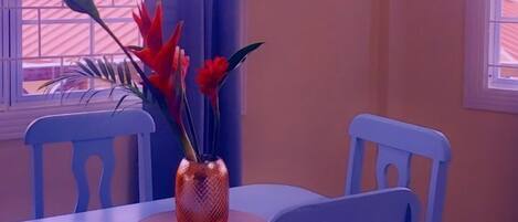 Un coin repas comprenant une table, des chaises, un vase avec des fleurs et un luminaire suspendu.