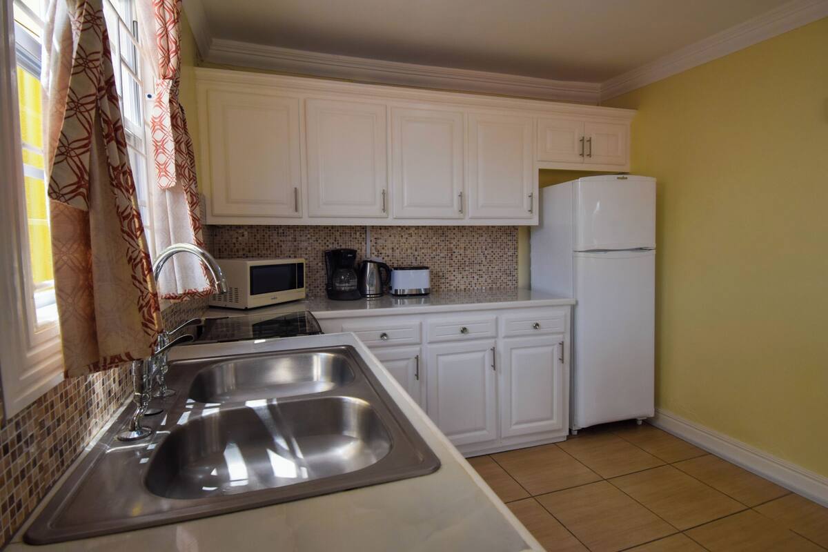 A kitchen with white cabinets, a stainless steel sink, a microwave, a coffee maker, and a refrigerator.